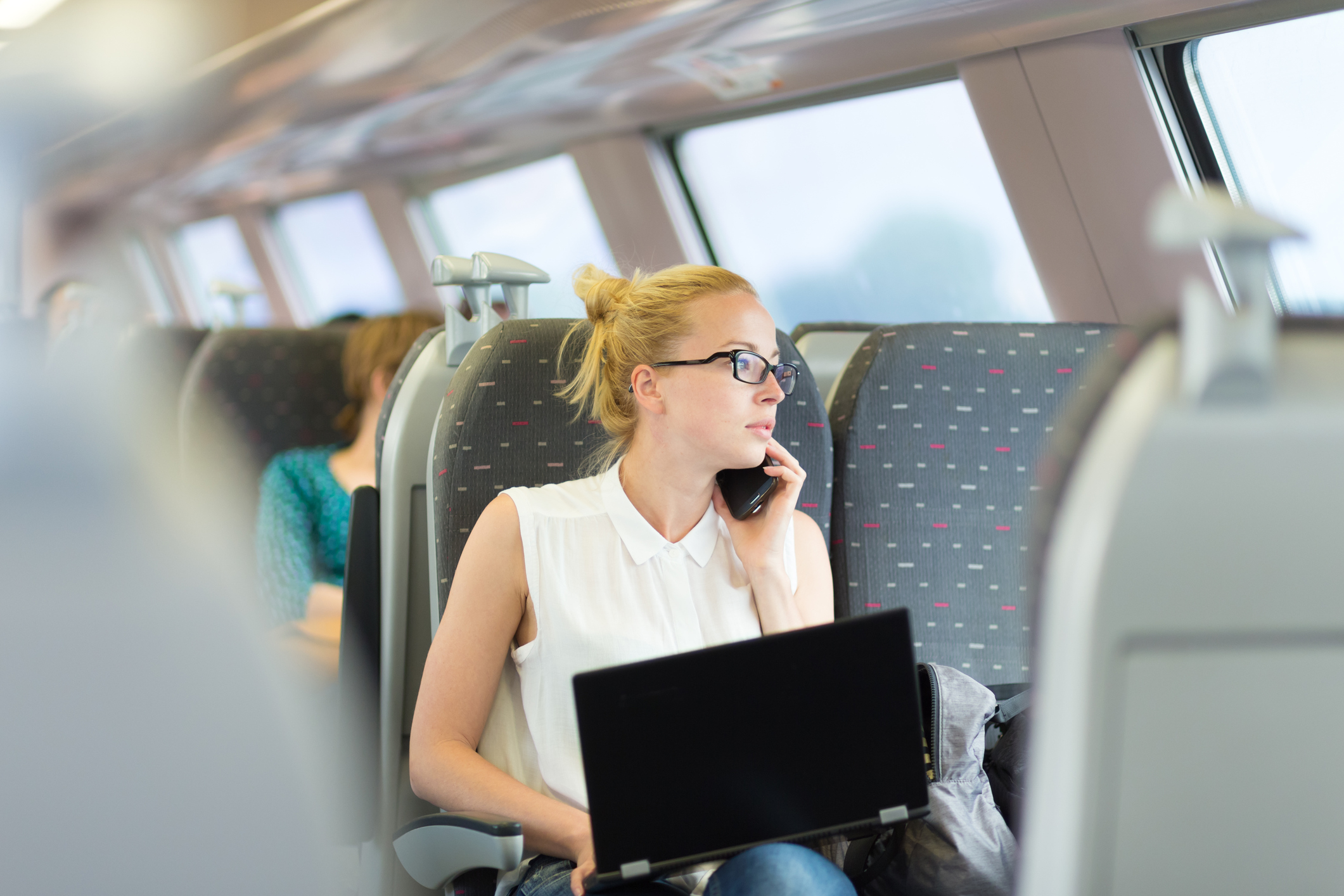 An image of a woman using her laptop and phone while seated on a train